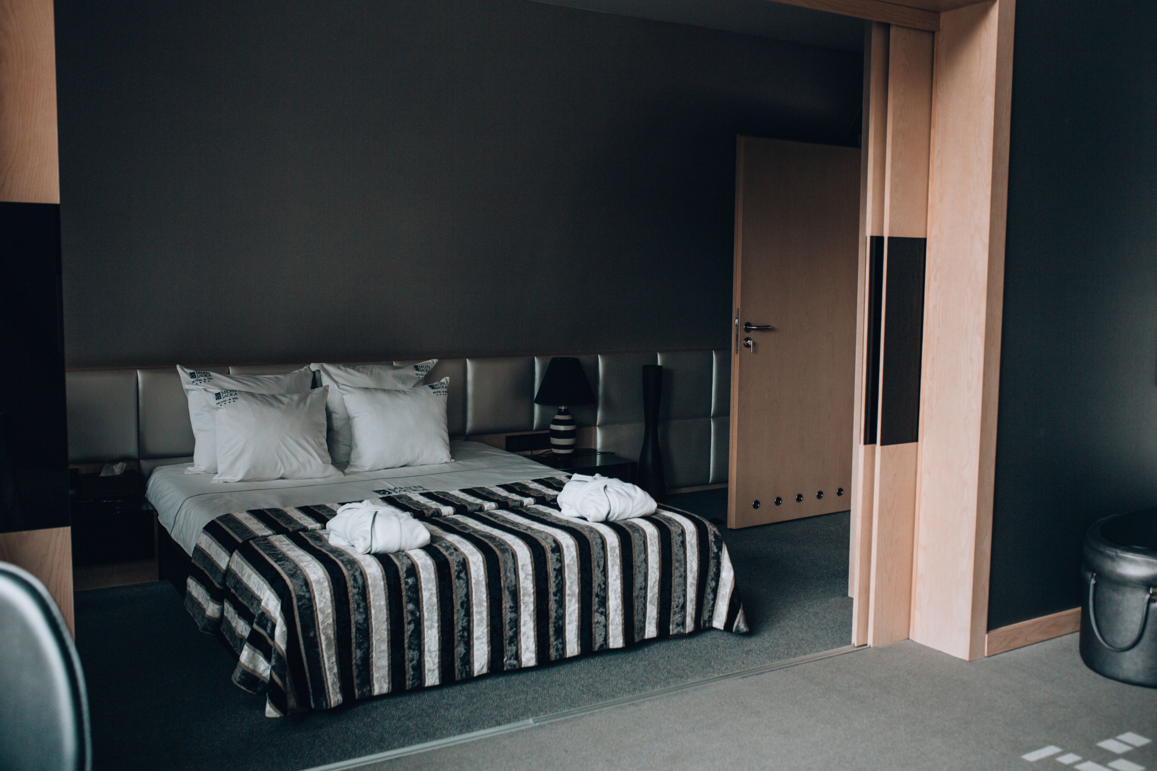 A modern hotel room with a large bed, a bedside table, a lamp, and a wardrobe.