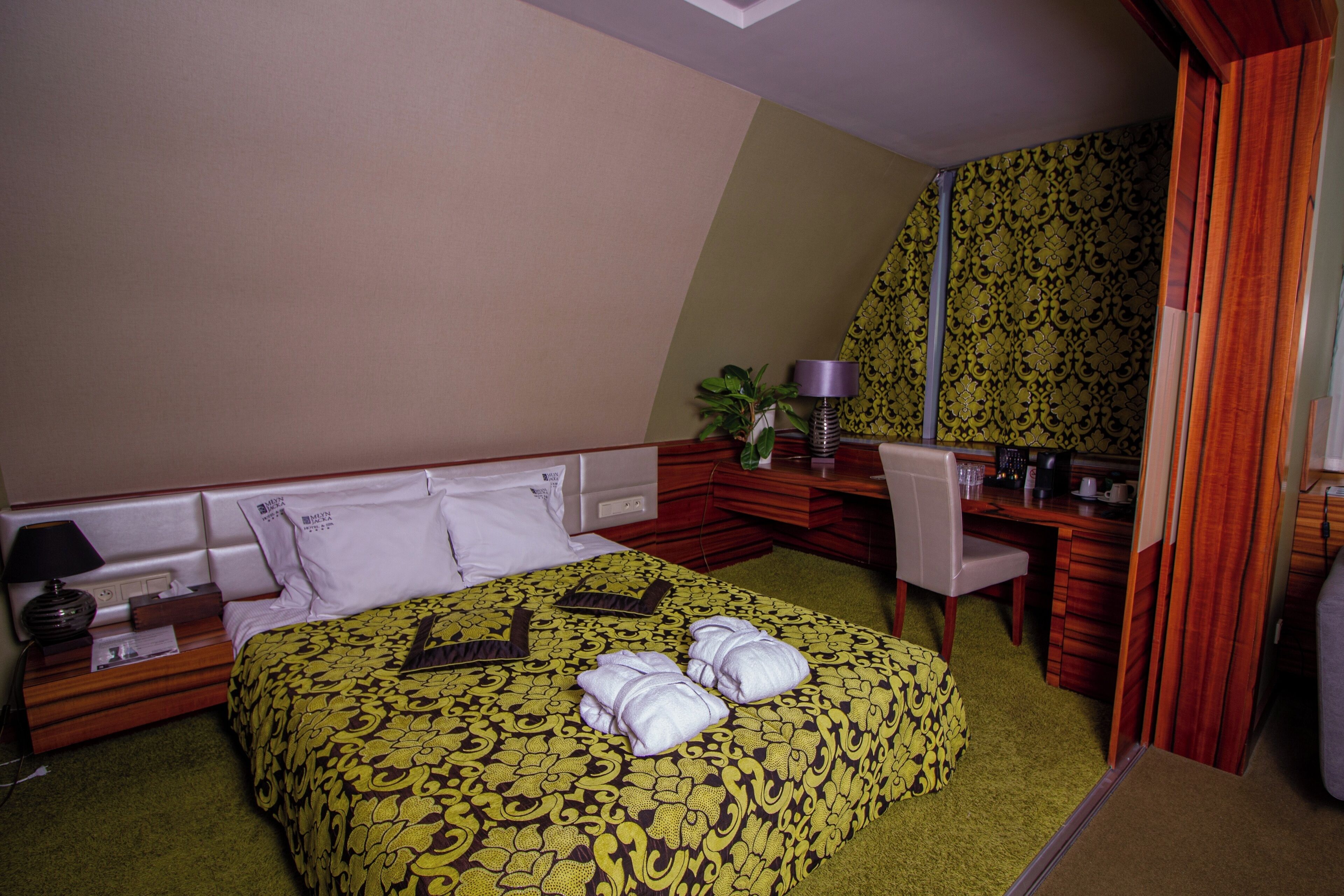 Una habitación de hotel con una cama grande, un escritorio, una silla, un espejo y una planta pequeña.