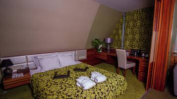 Una habitación de hotel con una cama grande, un escritorio, una silla, un espejo y una planta pequeña.