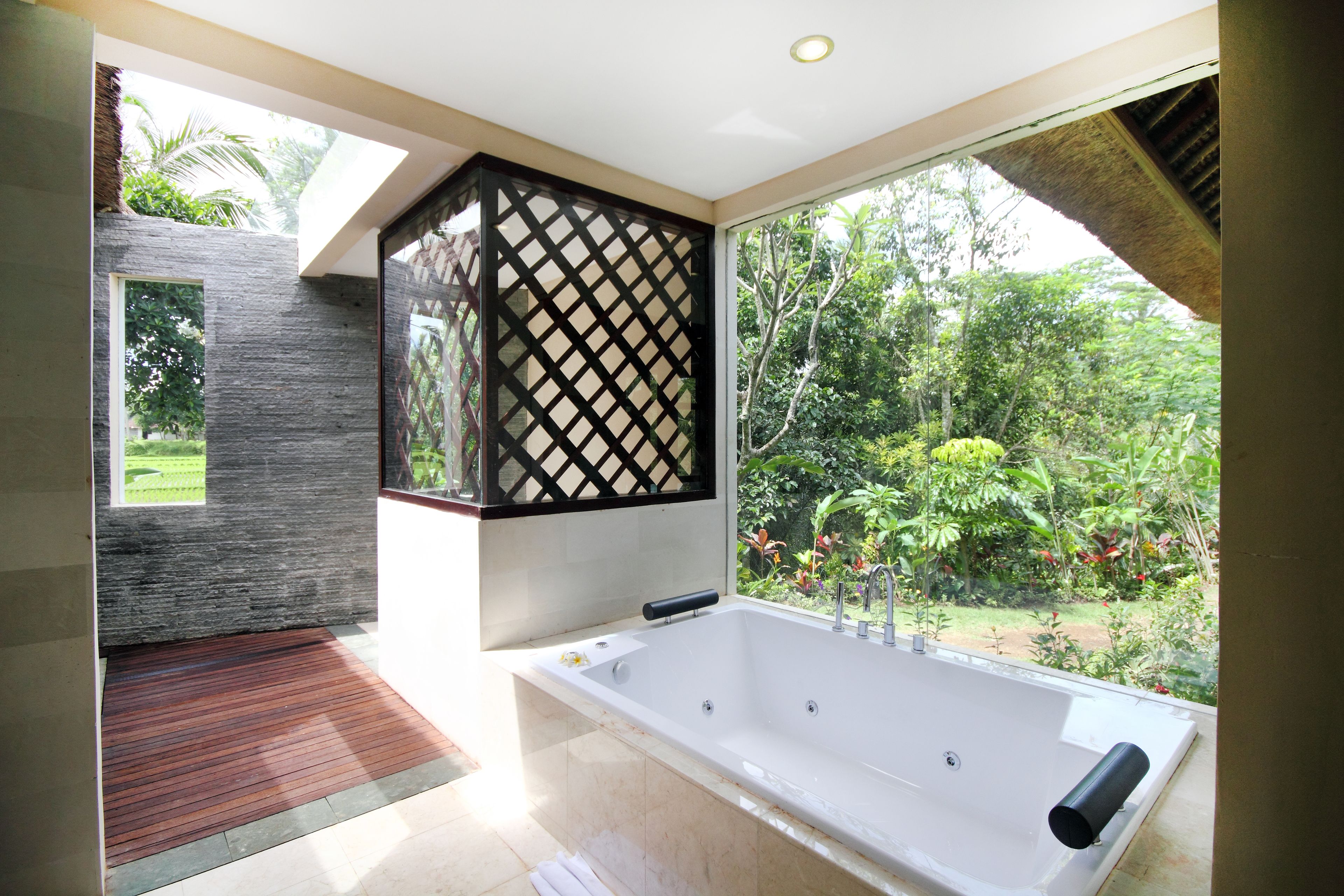 Une salle de bain moderne dotée d’une grande baignoire, d’une fenêtre offrant une vue sur la verdure et d’une cloison décorative noire au motif original.