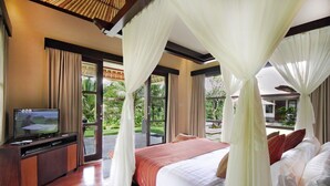 A bedroom with a bed, curtains, a television, and a view of the outdoors.
