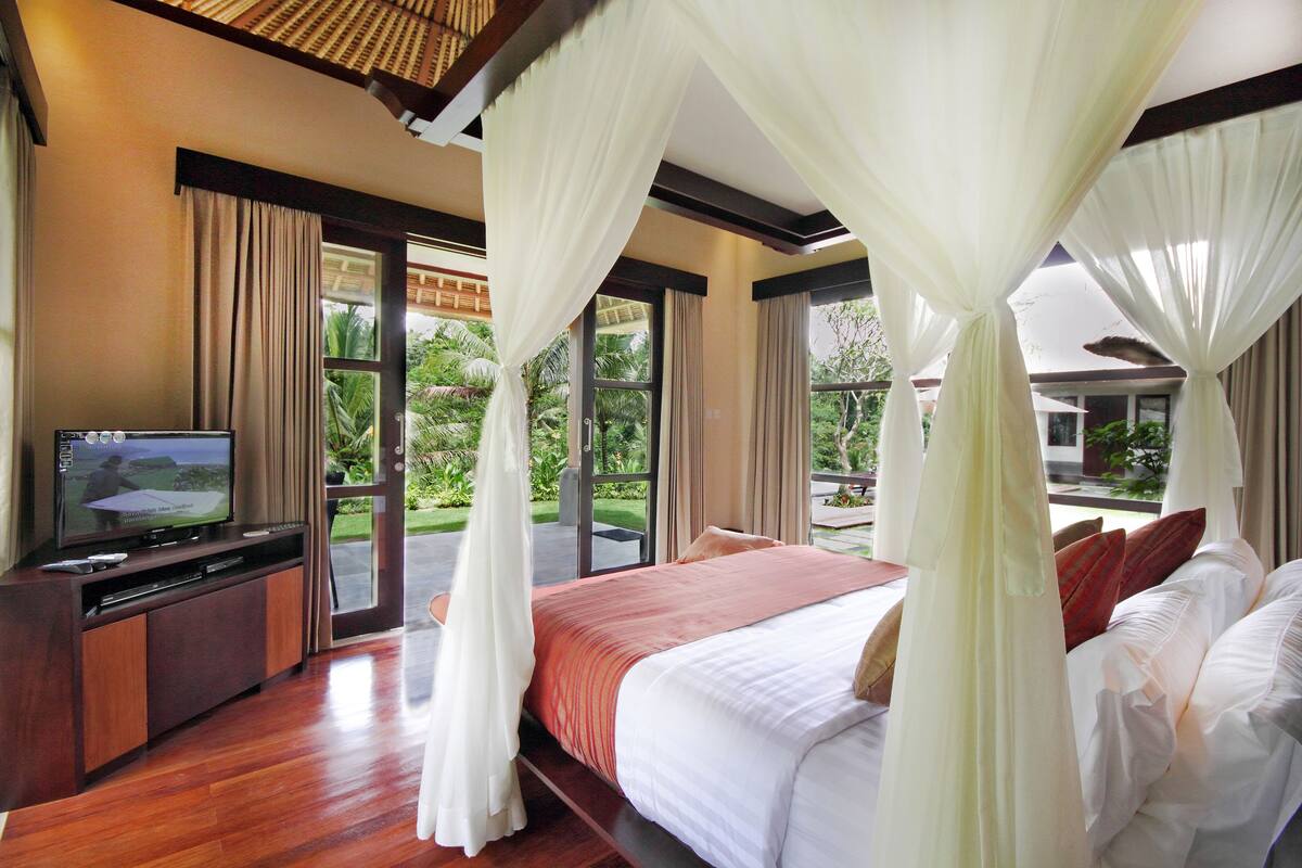 A bedroom with a bed, curtains, a television, and a view of the outdoors.