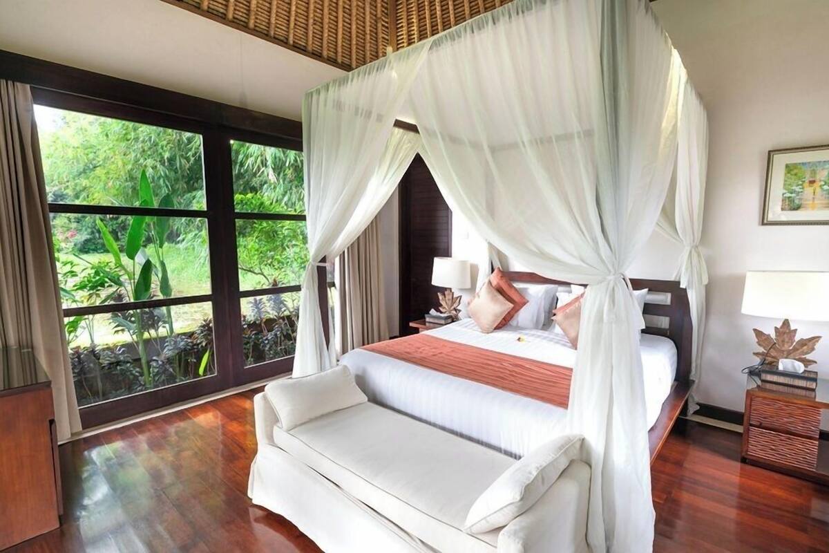 A bedroom with a canopy bed, large windows, and a view of greenery.