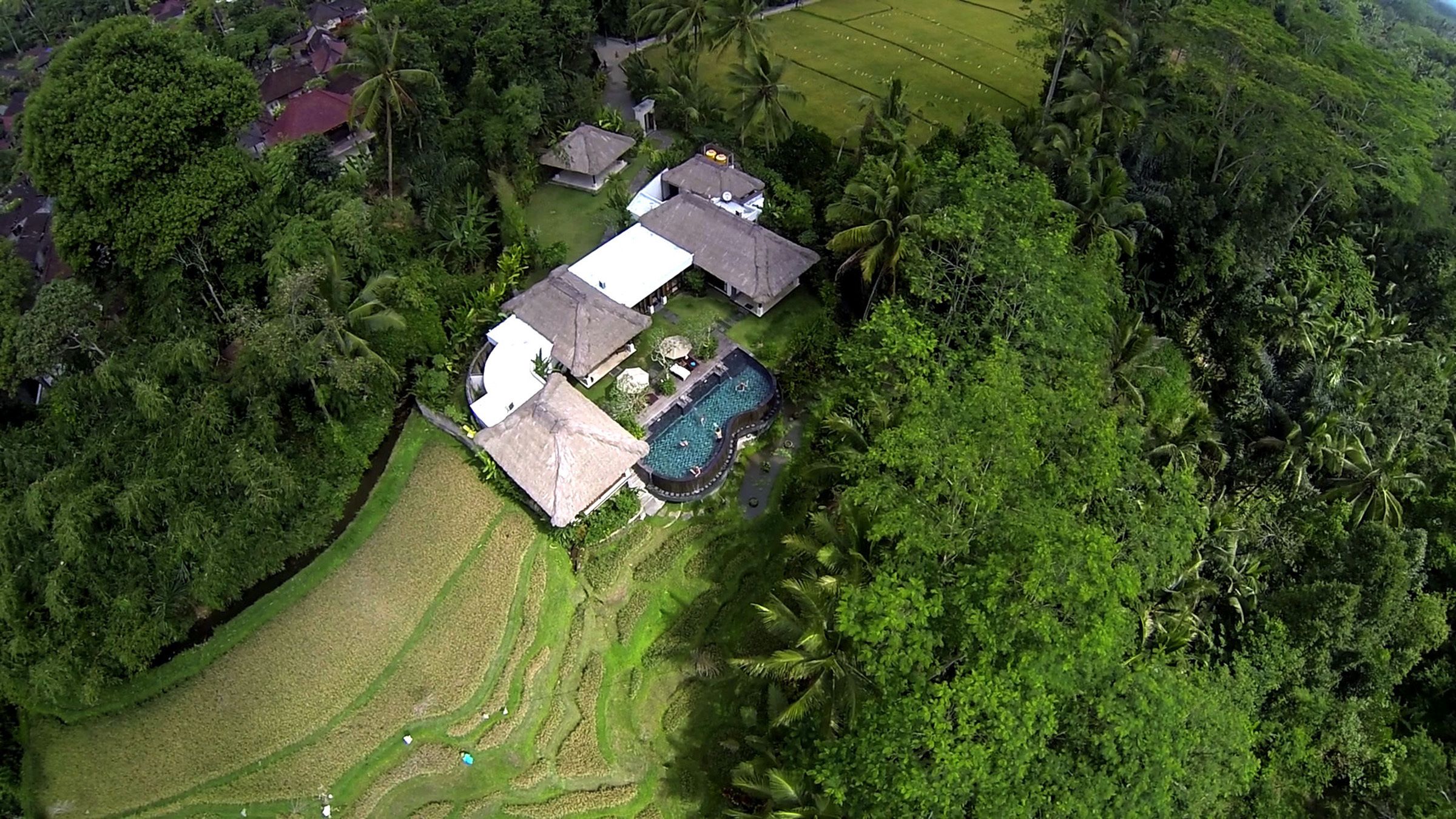 An aerial view of a property with a swimming pool, multiple buildings, and lush greenery.