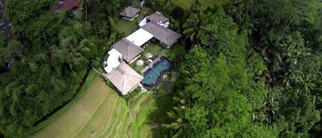 An aerial view of a property with a swimming pool, multiple buildings, and lush greenery.