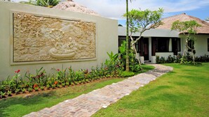 A landscaped garden with a stone pathway leading to a building with a thatched roof.