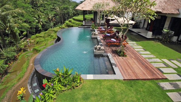 A swimming pool with a wooden deck, lounge chairs, and a thatched-roof structure.
