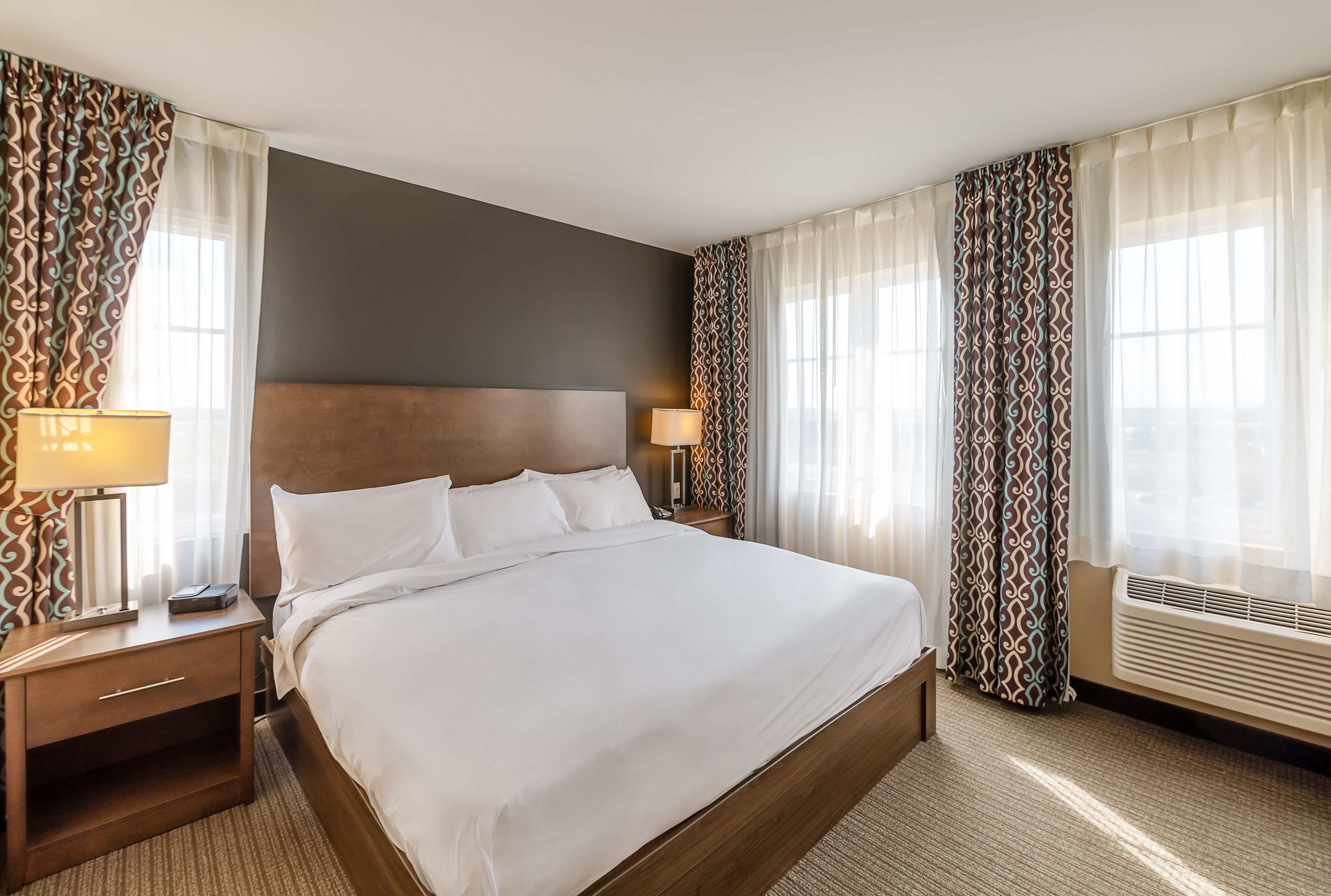 A hotel room with a large bed, two bedside tables with lamps, a headboard, and a window with curtains.
