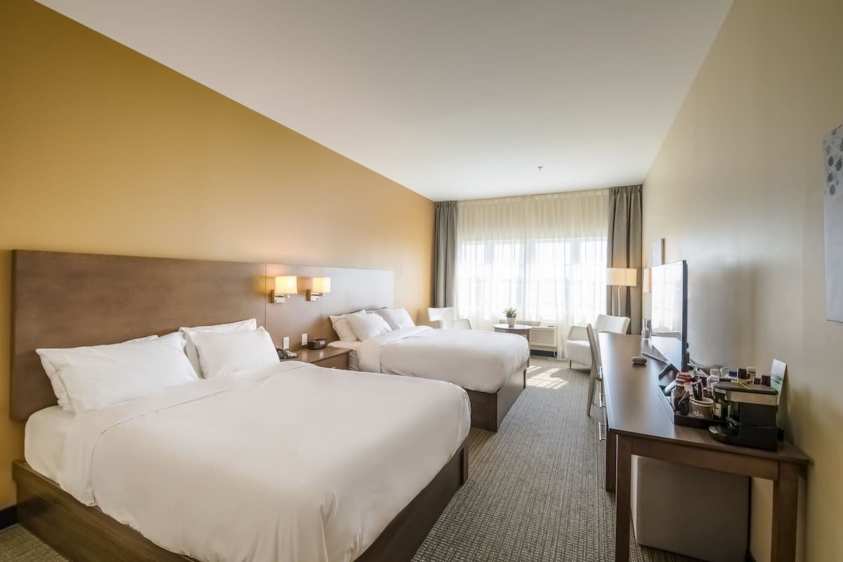 A hotel room with two beds, a desk, and a TV.