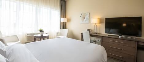 Una habitación de hotel con una cama grande, un escritorio con televisor, una silla y una lámpara.
