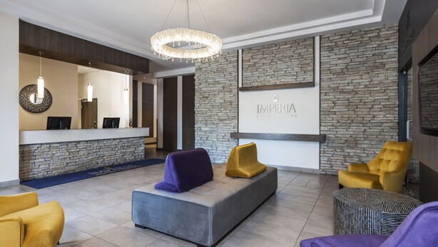 A modern lobby with a reception desk, stone wall, and seating area with yellow and purple chairs. - Imperia Hotel & Suites Terrebonne (Terrebonne)
