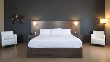 A modern hotel room with a large bed, two bedside tables, a wall-mounted lamp, and two white armchairs.