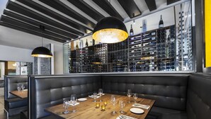 A restaurant with a wooden table set for dining, black leather booths, and a wine rack in the background. - Imperia Hotel & Suites Terrebonne (Terrebonne)