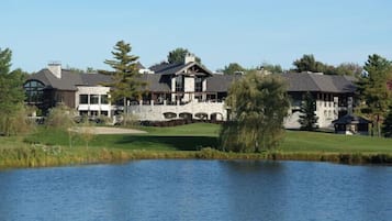 A large, multi-story building with a stone facade, arched windows, and a landscaped lawn with a pond.