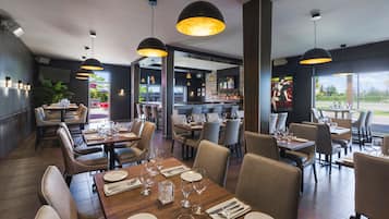 Ein Restaurant mit mehreren gedeckten Tischen für Gäste, das ein modernes Interieur mit Pendelleuchten und Blick ins Freie bietet.