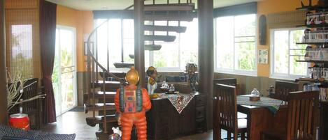 A spacious living room with a high ceiling, a staircase, and a dining area with wooden furniture.