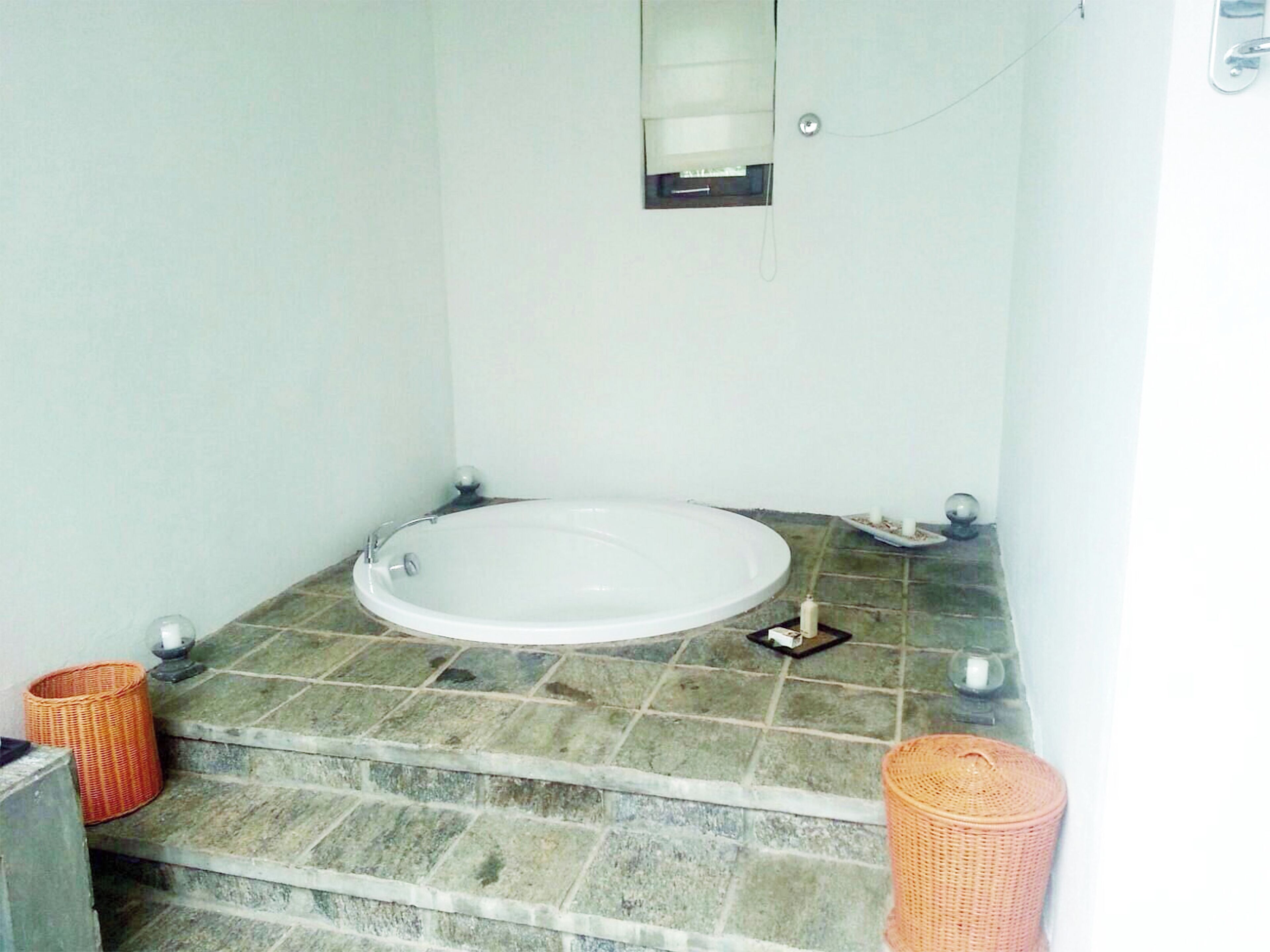 A bathroom with a bathtub, stone-tiled floor, and two wicker baskets.