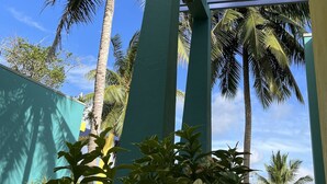 Una estructura con pilares verdes y techo azul, rodeada de palmeras y otra vegetación.