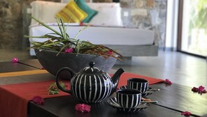 Una habitación moderna con una pared de piedra, un sofá con un cojín colorido, una tetera a rayas negras y blancas, y tazas a juego sobre una mesa.