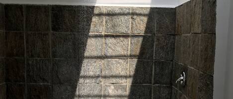 A stone-walled shower with a rain showerhead, a white pedestal, and a stone basin.
