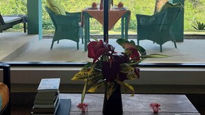 Una habitación con un ventanal grande que da a un paisaje tropical, una mesa de comedor con sillas y un florero con flores sobre una mesa.