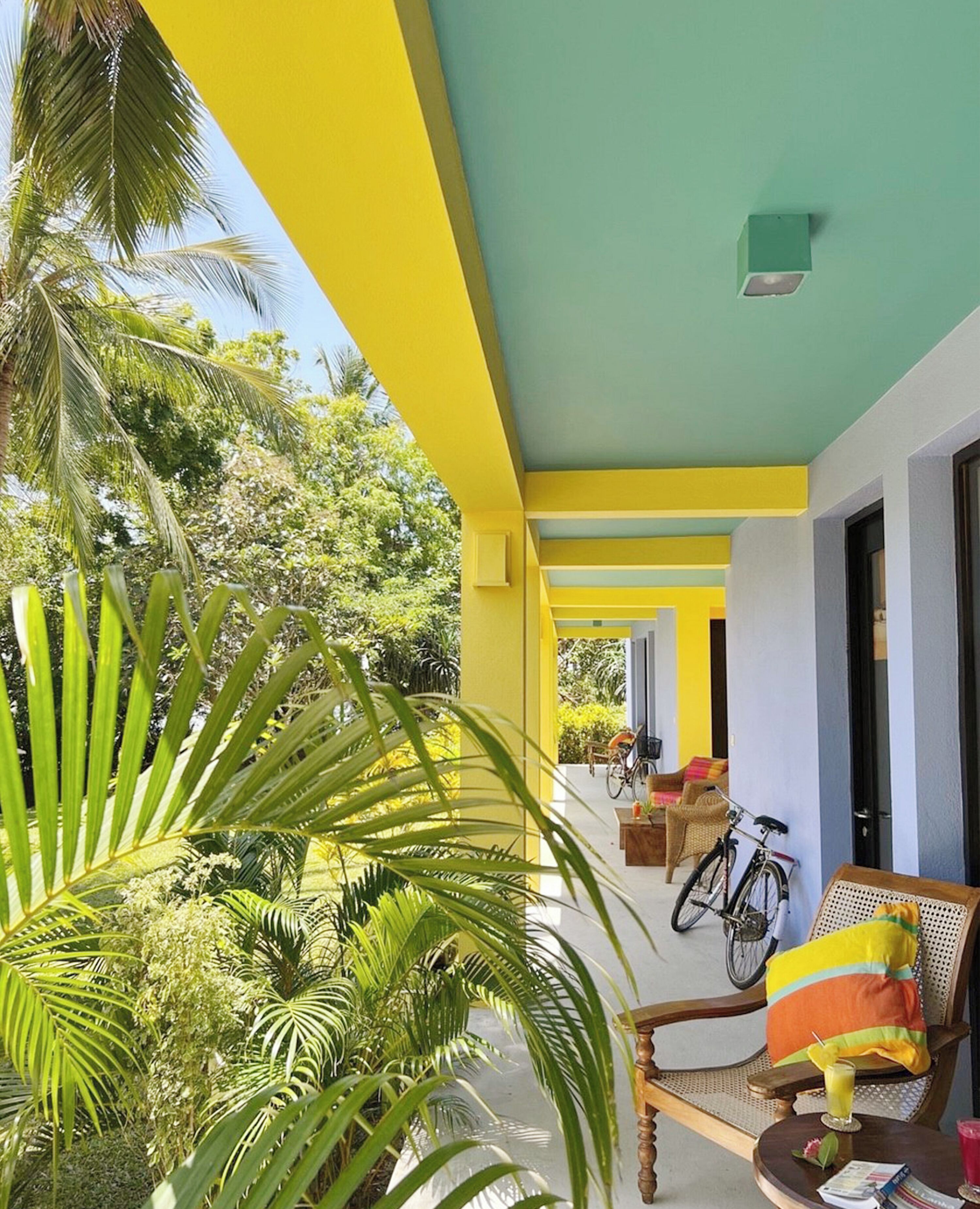 A brightly colored building with yellow and green walls, a covered outdoor seating area with wicker furniture, and a bicycle.
