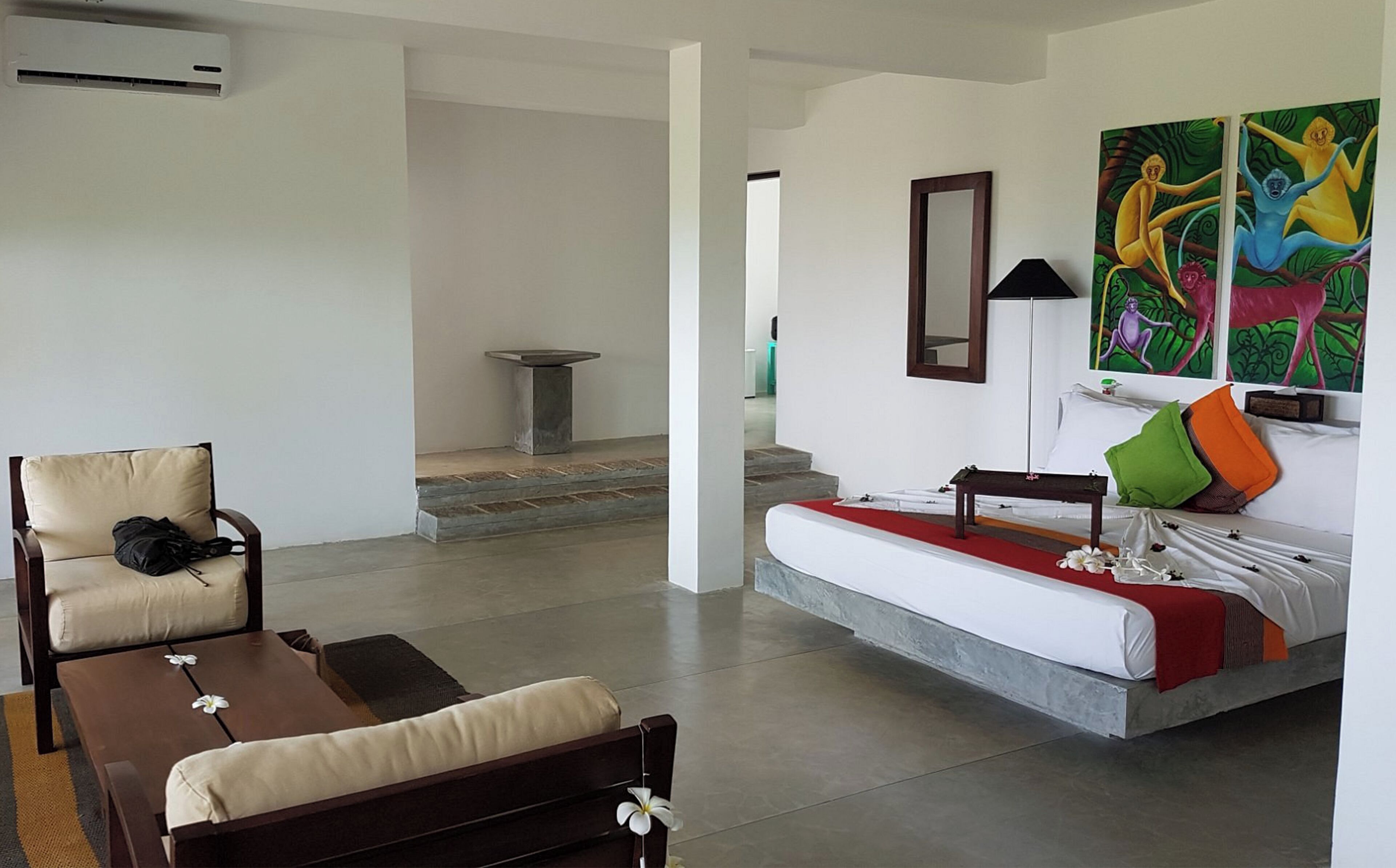 Habitación de hotel moderna con cama, sofá, sillón y una mesita. Se observa un cuadro en la pared y una ventana con vistas al exterior.