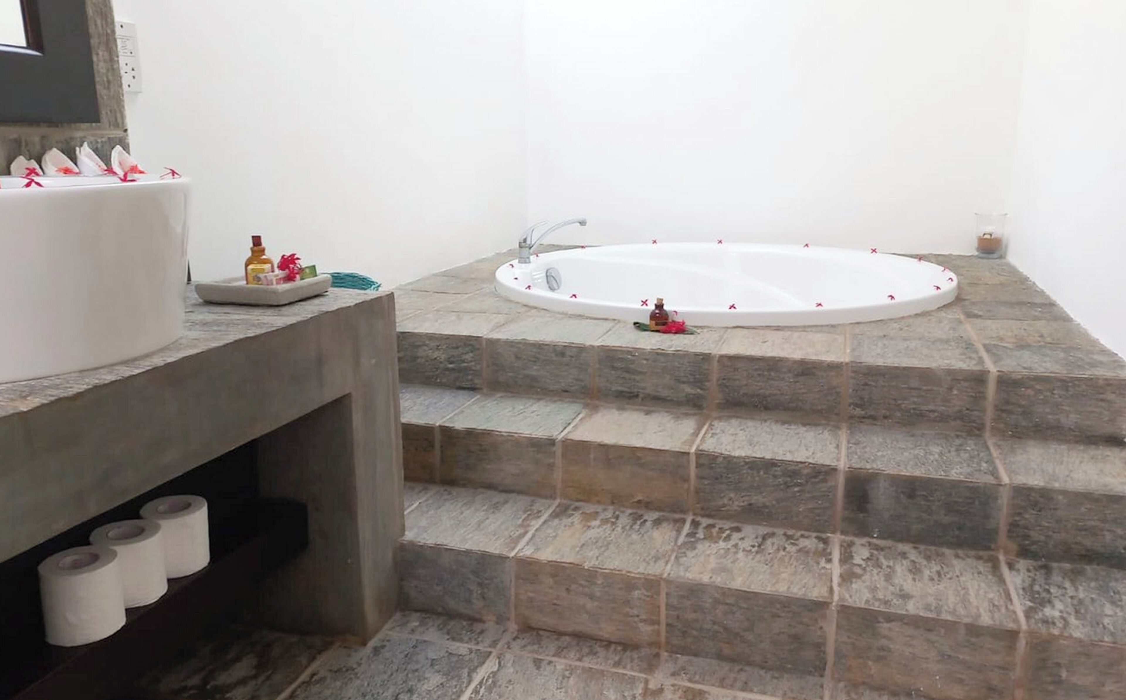 Ein Badezimmer mit Steinfliesen, einer weißen Badewanne und einem Waschbecken mit Pflegeprodukten.