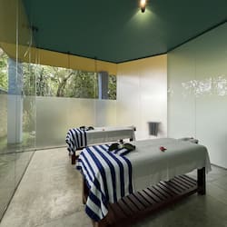 Two beds and a bench sit in a clean, geometric space with a large glass door leading to an outdoor area.