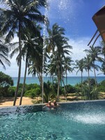 Vista despejada de una piscina con agua salpicando, rodeada de palmeras y vista al océano.
