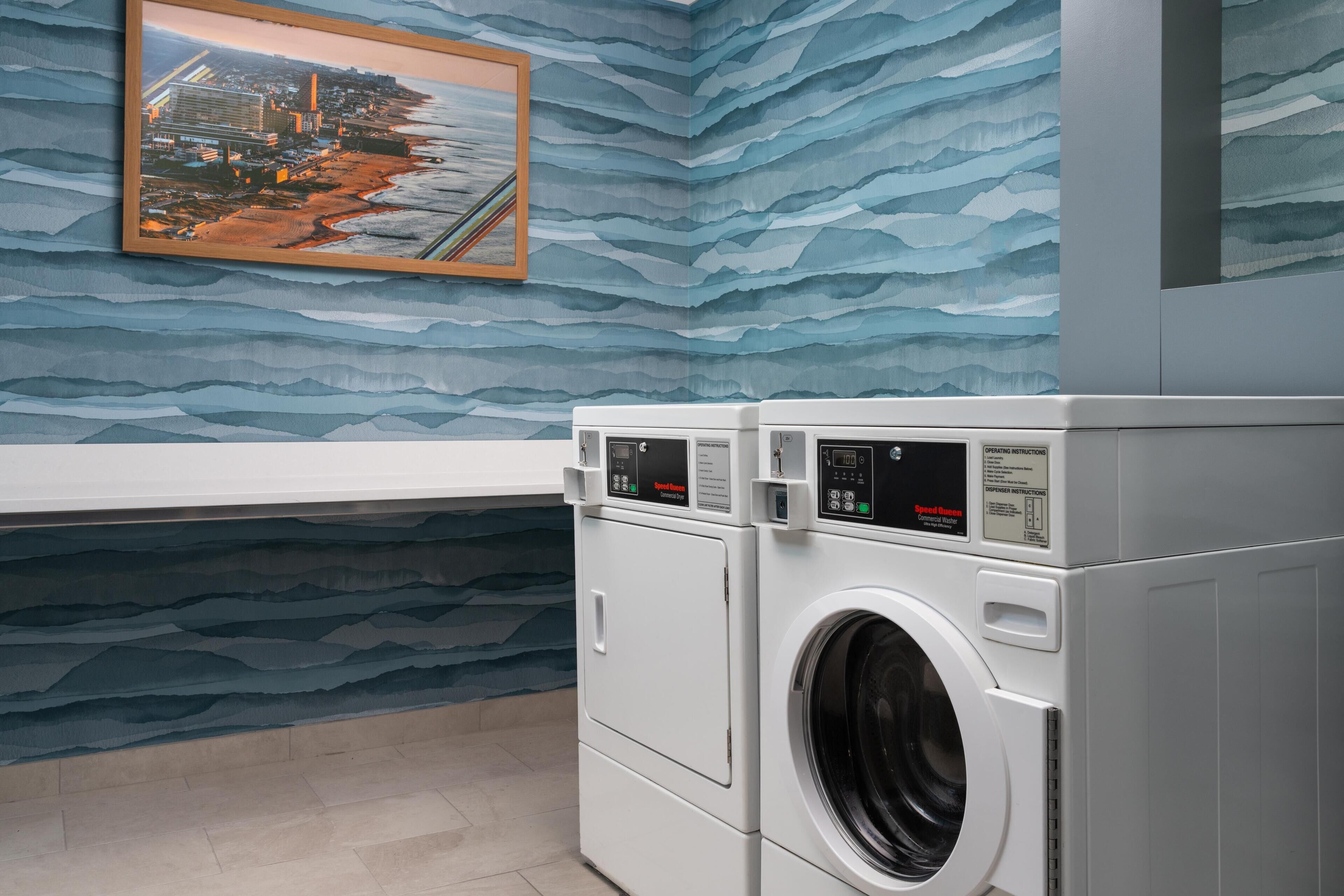 Een wasruimte met een grote wasmachine en droger, een stadsgezicht in een lijst en een behang met patroon.