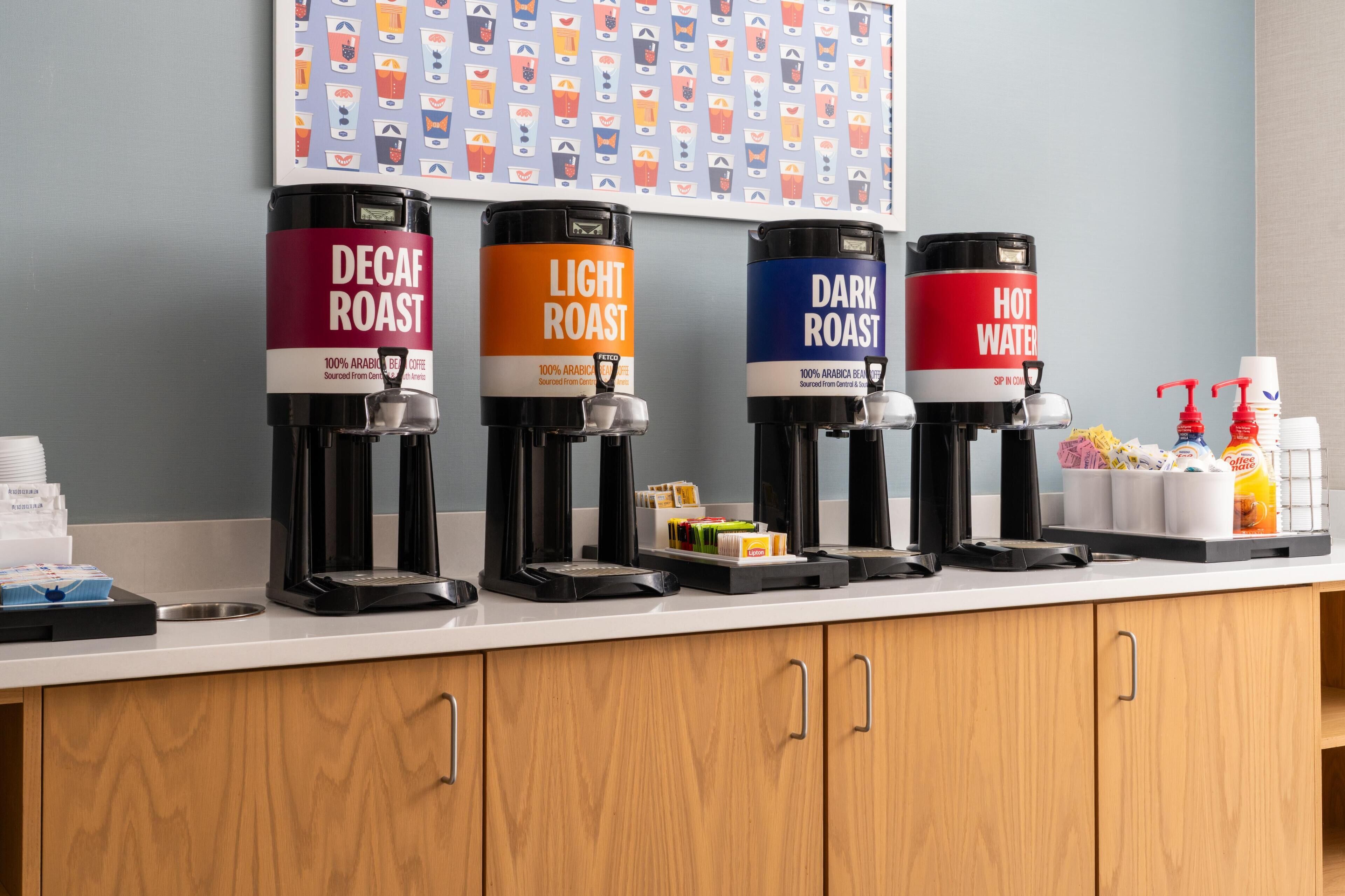 A coffee station with four dispensers labeled Decaf Roast, Light Roast, Dark Roast, and Hot Water.