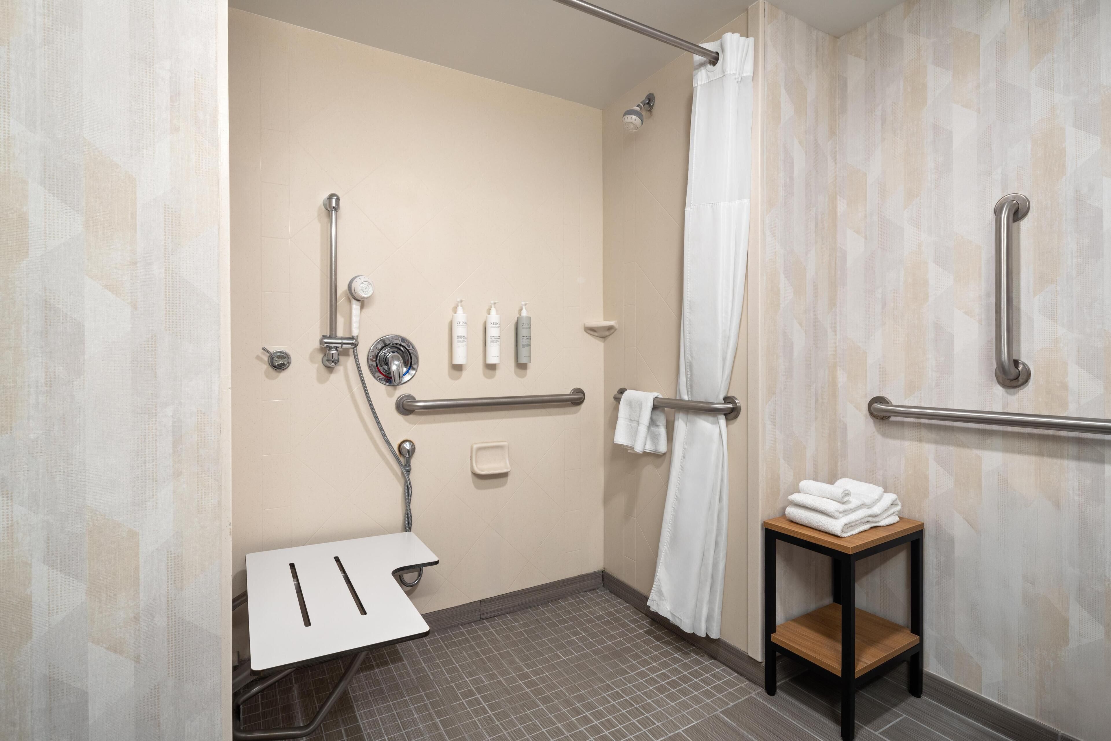 A handicap-accessible bathroom with a shower, grab bars, a towel rack, and a small table with towels.