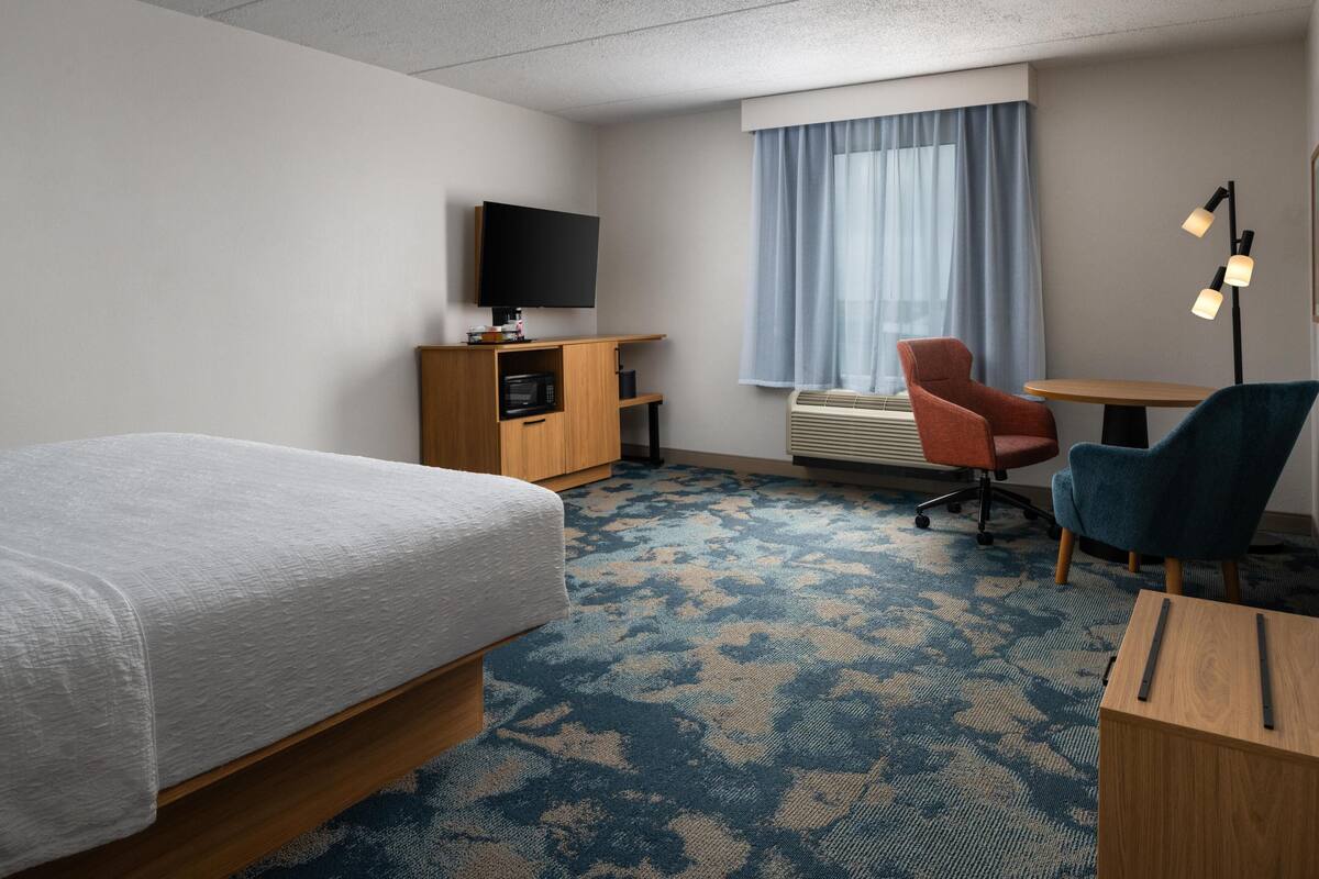 A hotel room with a bed, a desk, a chair, a television, and a window with curtains.