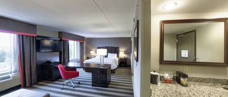 Une chambre d’hôtel comprenant un lit, un bureau, une chaise, une télévision, un miroir, une salle de bain et une fenêtre.