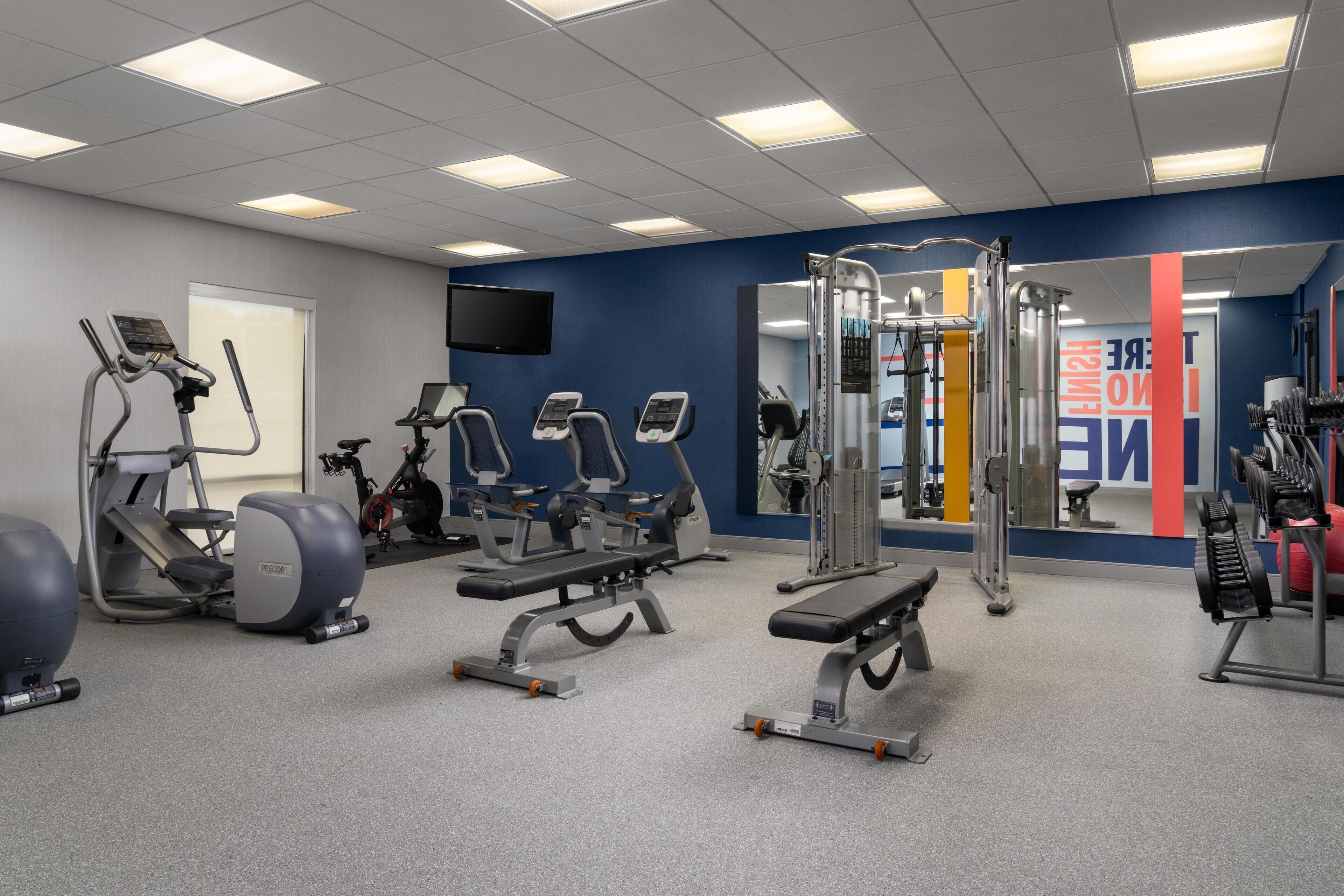 Une salle de sport équipée de tapis de course, d’appareils de musculation et d’un miroir.