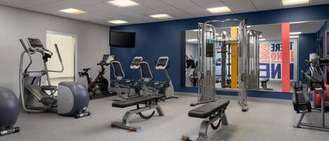 Une salle de sport équipée de tapis de course, d’appareils de musculation et d’un miroir.