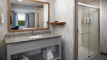 Un baño moderno con encimera de granito, un lavamanos, un espejo, cabina de ducha de vidrio y un perchero para toallas.
