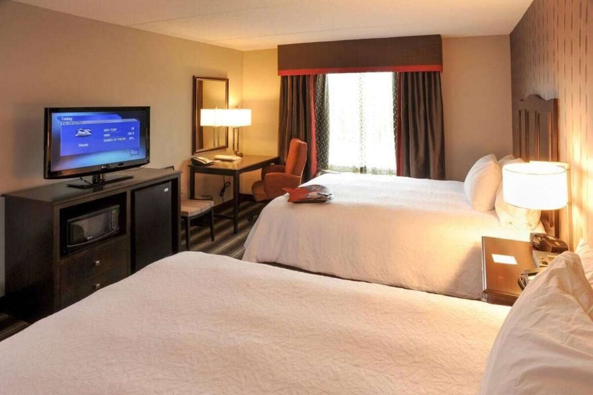 A hotel room with two beds, a desk with a chair, a television, and a window with curtains.