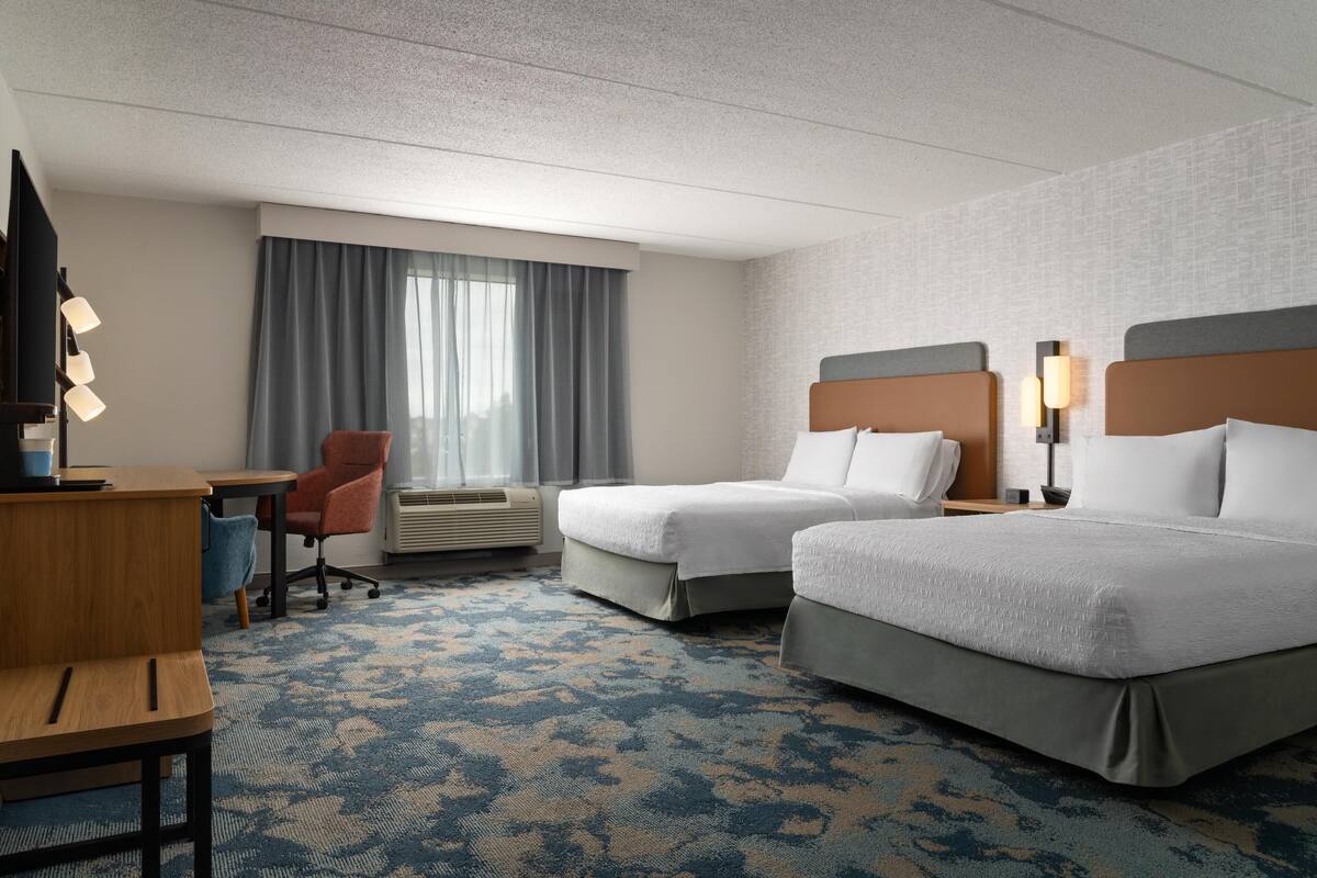 A hotel room with two beds, a desk, a chair, and a TV.