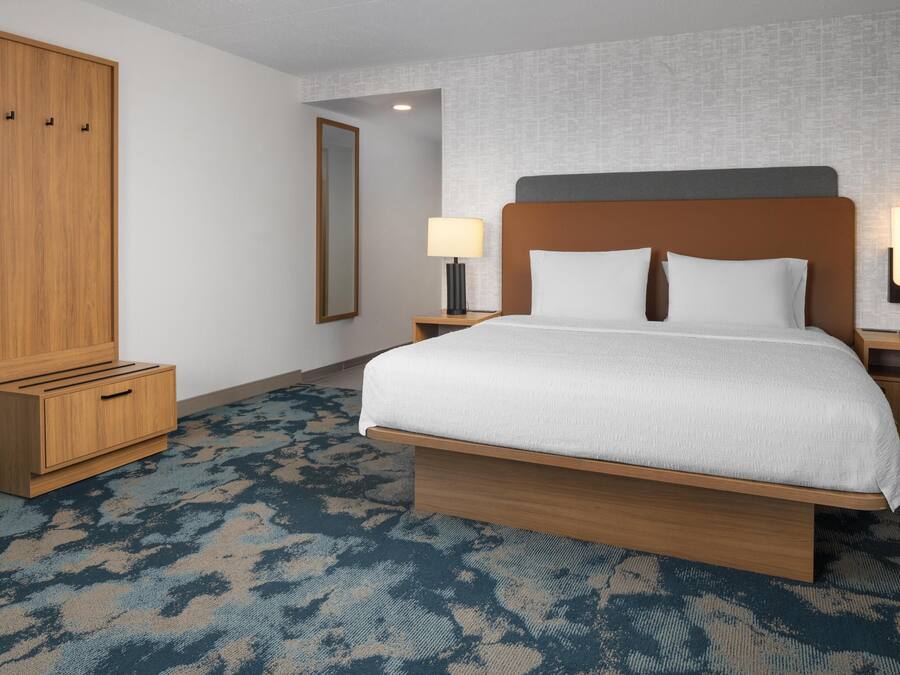 Ein Hotelzimmer mit einem großen Bett, einem Holzschrank, Nachttischen mit Lampen und einem gemusterten Teppich.