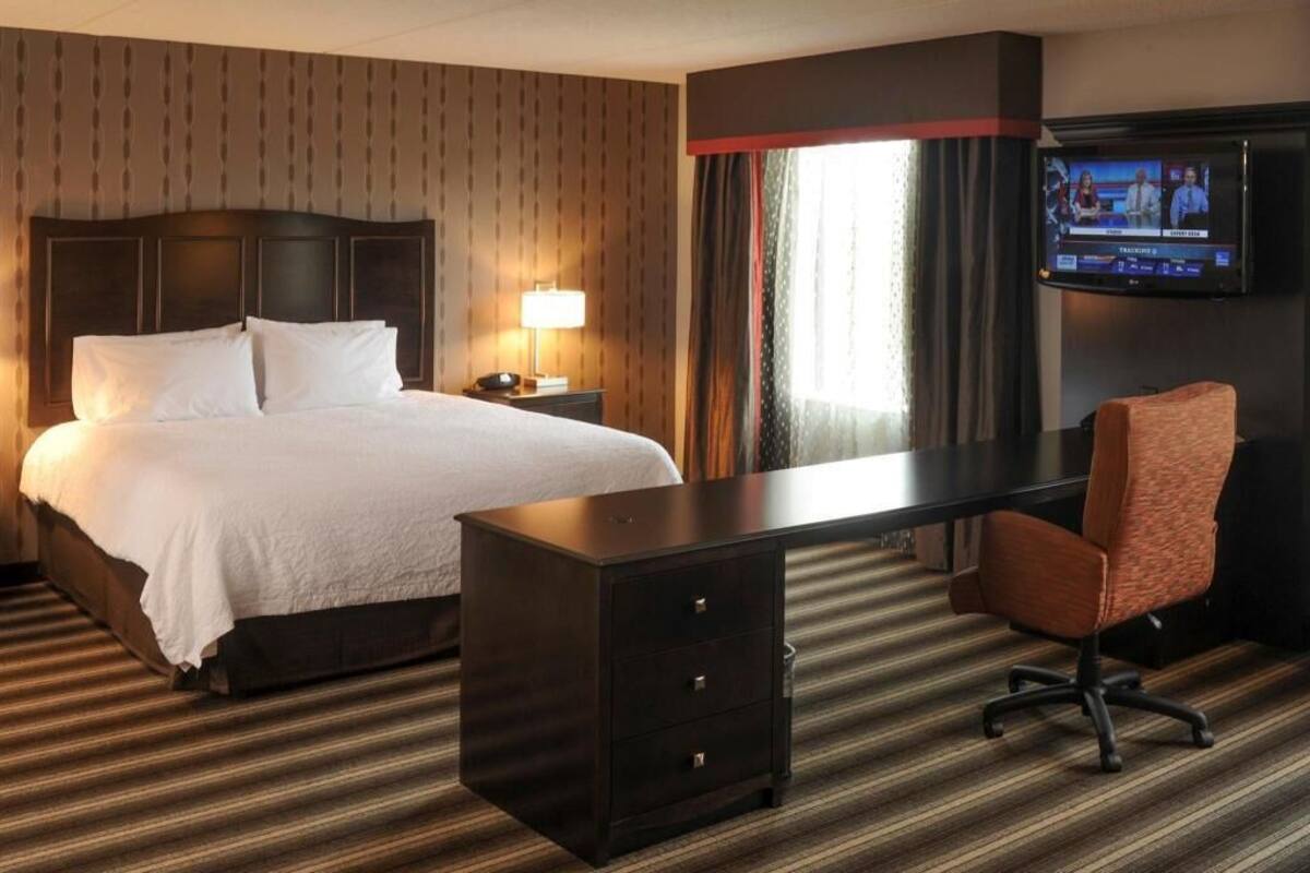 A hotel room with a bed, a desk, a chair, a television, and a window with curtains.