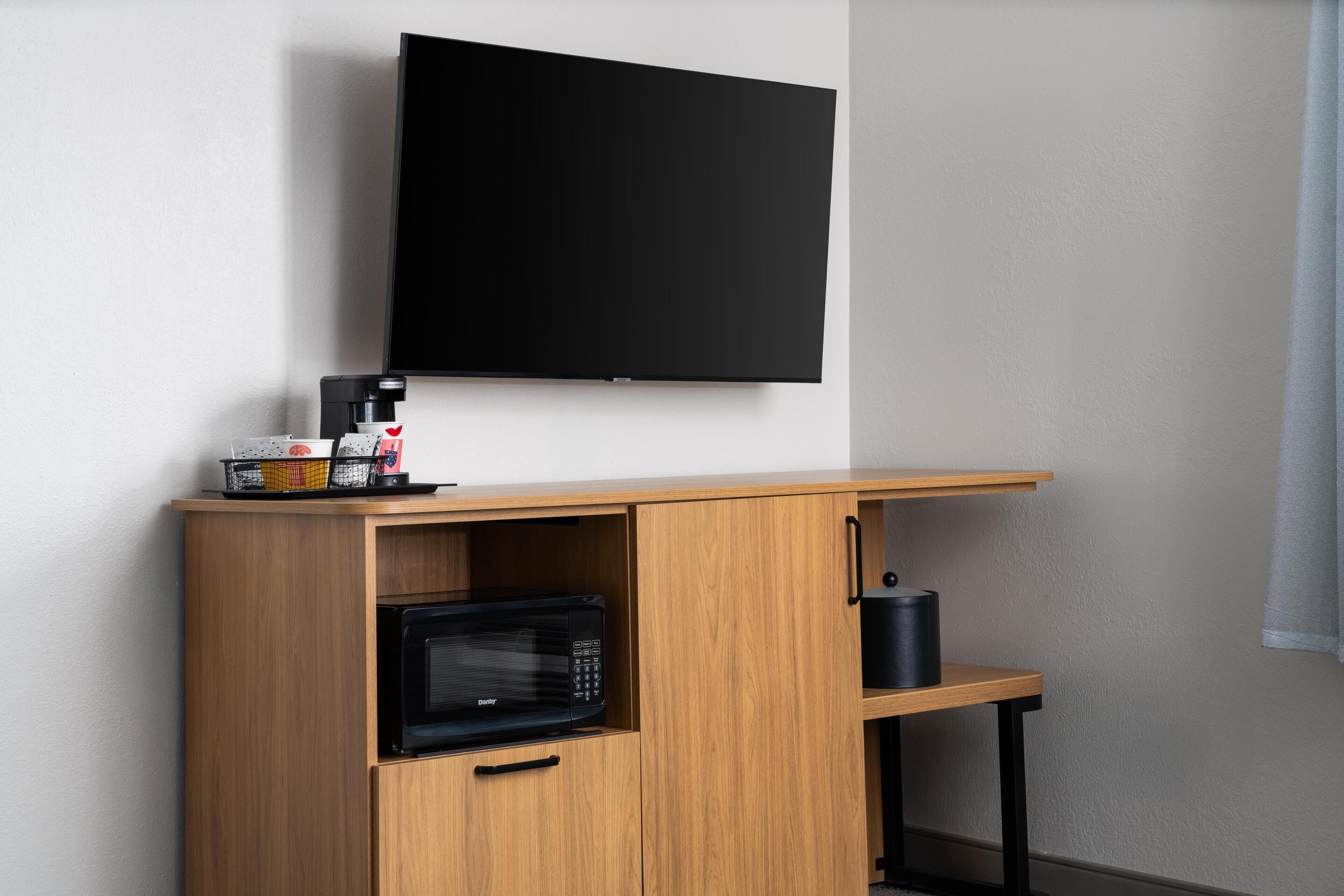 Una kitchenette compacta con microondas, cafetera y televisor de pantalla plana montado en la pared.
