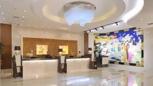 Zona de recepción de hotel con diseño moderno, que incluye un mostrador de recepción, un cuadro grande colgado en la pared y un plafón con una lámpara circular.