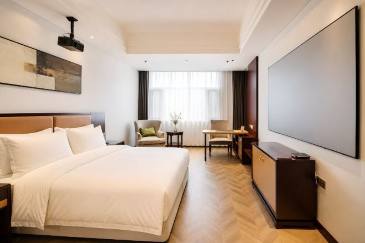 A hotel room with a large bed, a desk, a chair, and a flat-screen TV.