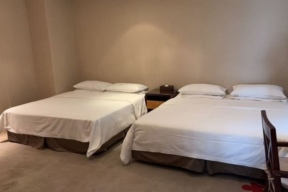 A room with two single beds, each with white bedding and a wooden nightstand.