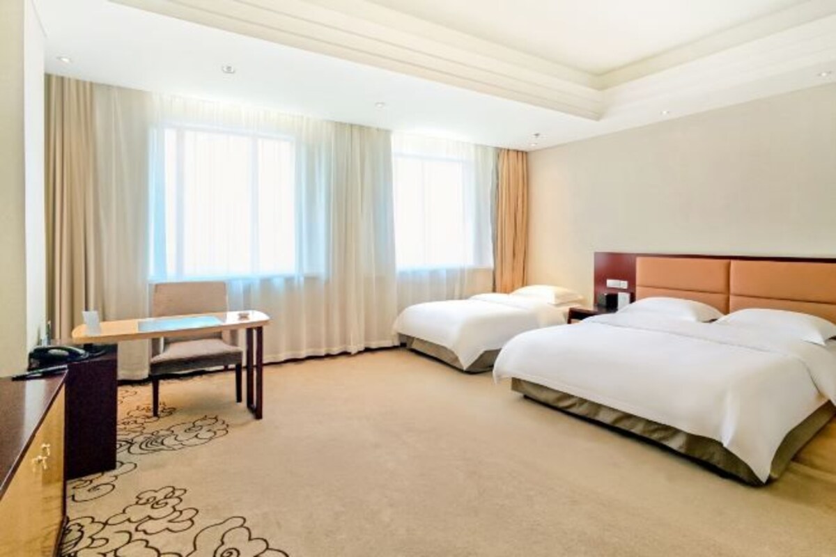 A hotel room with a desk, two beds, a headboard, and a carpet with a floral pattern.