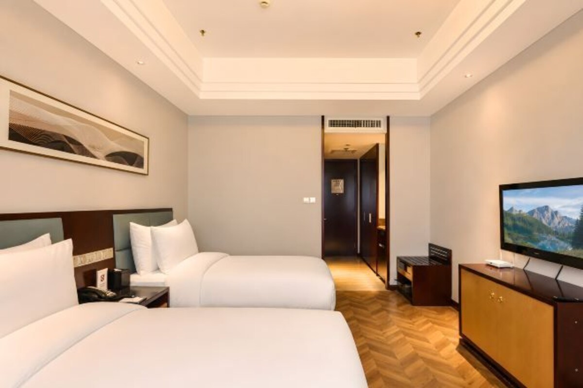 A hotel room with two beds, a television, and a wooden floor.