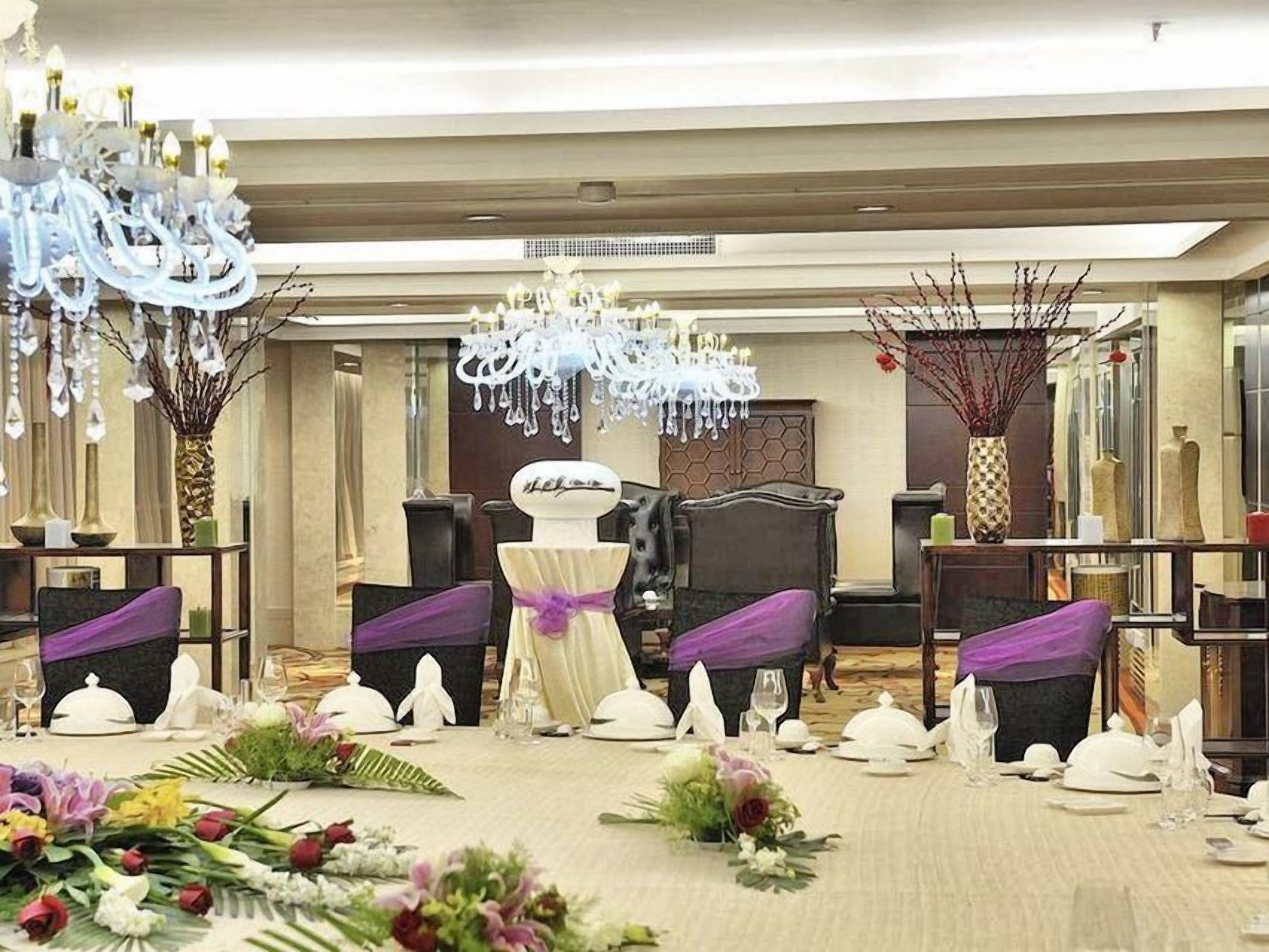 Salão de festas com mesas redondas, capas roxas para as cadeiras e um arranjo floral central.