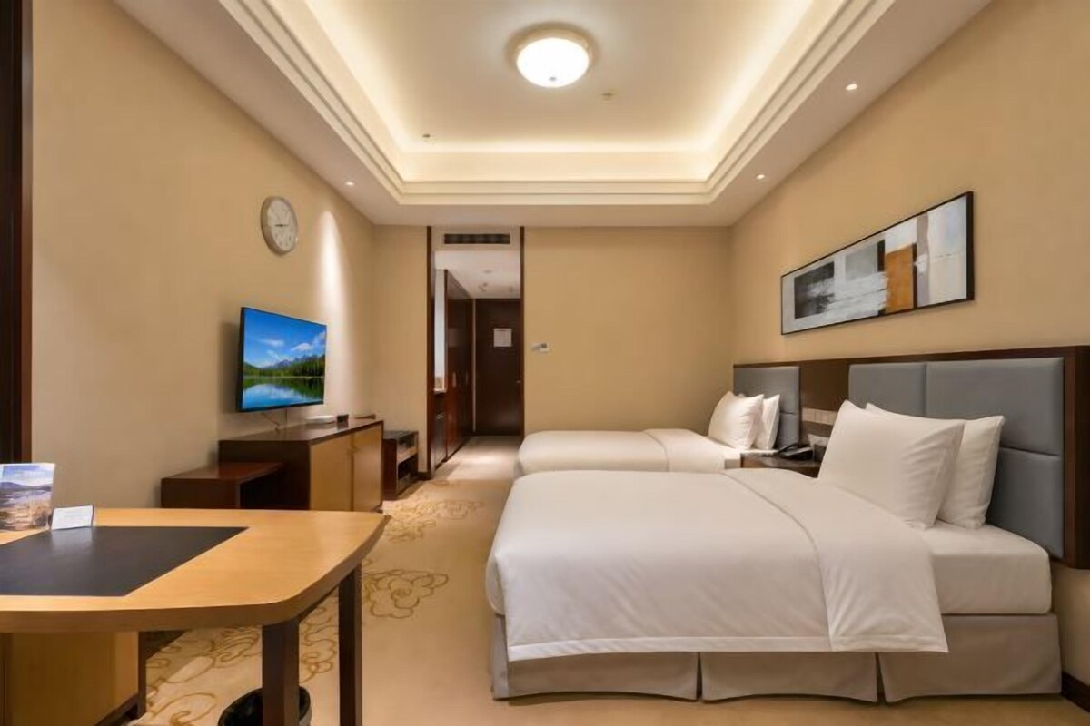 Una habitación de hotel con cama, mesita de noche, televisor y un cuadro en la pared.